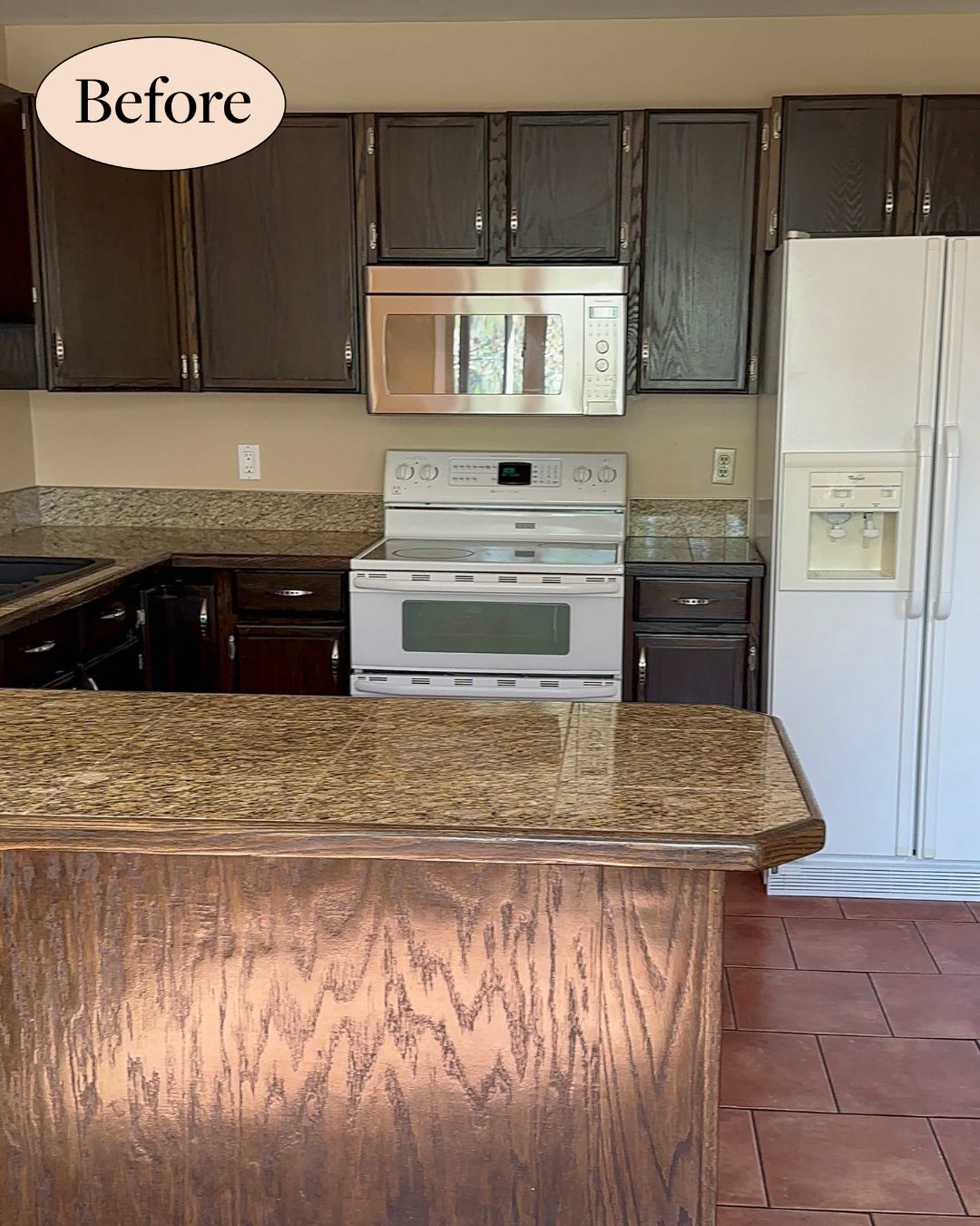 A before photo of a kitchen renovation featuring dark espresso oak cabinets, mottled granite countertops, white appliances including a stove and a refrigerator with an ice dispenser, and a beige wall with red-brown tile flooring. A wood-grained island with a bevel-edged granite countertop stands in the foreground, and a oval graphic reading "Before" appears in the top-left corner.